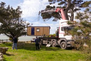 The cabin is lifted from the flat-bed truck using the truck's own crane